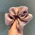 Pink satin scrunchie with sparkling rhinestone edges held against a grey background - Pink