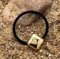 Dettaglio dell'elastico per capelli nero con perla quadrata in metallo dorato su sassi - Quadrato Oro