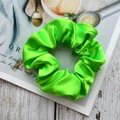 Luminous bright green satin scrunchie hair tie placed on an open magazine display - Fresh Green