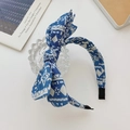 Blue denim style bow headband with white geometric patterns on a glass display stand - Floral
