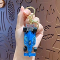 Blue mini racing car keychain with golden metal ring and hook shown in hand - Blue