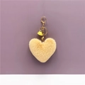 Detail view of heart-shaped yellow faux fur keychain with gold clasp and tassel - Beige