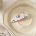 Dettaglio molletta per capelli in acrilico rosa trasparente con fiori su piatto di ceramica - Floreale Rosa Blu