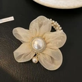 Close-up of champagne organza flower hair tie with pearl center and rhinestone details - Beige