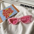 Close-up of pink jelly cat-eye sunglasses on white fabric with music-themed decor - Cat Eye / Pink Frame Pink Lens