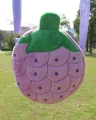 Detail of pink fruit plush crossbody bag with green leaf decoration on green grass - Grapes