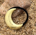 Detailaufnahme von goldenem Glitzermond-Haargummi auf Sand und rötlichem Stein - Mond