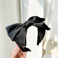 Detailed view of a black satin headband with a large bow showing fabric texture - Black
