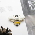 Vista macro de un broche de abeja con perlas y diamantes sobre una revista artística - Estilo Abeja Perla Base Dorada