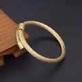 Detailed view of the golden twisted steel wire cable bracelet on a dark wooden base - Round End Bangle Gold