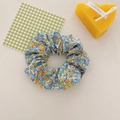 Blue floral scrunchie with yellow and orange patterns on a cream fabric surface - Blue Chamomile