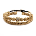 Detailansicht eines goldenen Totenkopf-Charms mit Kristallaugen am geflochtenen Armband - Gold Offener Armreif + Totenkopf Armband