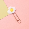 Poached egg shaped metal bookmark clip with a creative cartoon design on a pink surface - Egg