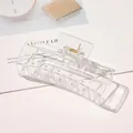 Detailed view of a large clear acrylic hair claw clip with golden metal spring on a magazine - 10.5cm Rectangular - Glossy Transparent