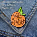 Just Peachy fruit enamel pin in orange and green on blue denim fabric background - Peach