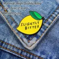 Enamel lemon pin with Slightly Bitter text pinned on dark blue denim jacket fabric - Lemon