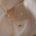 Elegant gold titanium steel necklace with a smooth bean pendant on beige silk background - Gold