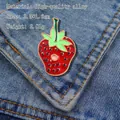 Detail of red strawberry enamel brooch with green leaves pinned on blue denim fabric - Strawberry