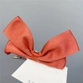 Macro detail of a large coral satin ribbon bow hair clip on a white display card - Duckbill Hair Clips / Caramel color