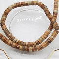 Macro detail of 6x3mm natural stone abacus beads in a gold-rimmed glass dish - Jasper