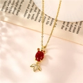 Titanium gold goldfish necklace with a large red garnet stone on a blurred book background - Cross Chain Goldfish Style / Gold/Red