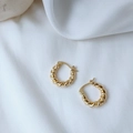 Detail von gedrehten 14K vergoldeten Creolen auf elegantem weißem Seidenhintergrund - Gold