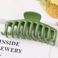 Detail of a large green geometric claw clip on a minimal decorative card background - Matte Green