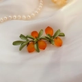 Gros plan détaillé d'une broche orange avec feuilles vertes sur tissu en soie - Broche Orange