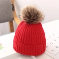 Detail of red knit baby hat with a large fluffy faux fur pompom in a white box - 2-24 Months / Standard / Red