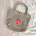 Detailansicht des Erdbeerdrucks und Metalldruckknopfs auf der beigen Canvas-Tasche - Graue Erdbeere