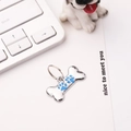 Detail of bone-shaped silver metal pet tag with blue paw prints on white surface - 30*15mm / Blue