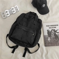 Minimalist black canvas backpack with dual top handles shown in an aesthetic lifestyle setting - Without Pendant / Black