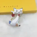 Detailed close-up of a white enamel Egyptian cat brooch with floral accents on a book - White Patterned Cat