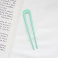 Minimalist mint green U-shaped hair pin for bun styling on a white fabric background - Creamy Green