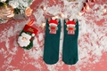 Close-up of green knitted Christmas socks with 3D reindeer decor and festive background - One Size / Dark Green Reindeer