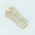 Macro detail of curved wide-tooth acetate hair comb with cream marble texture finish - Off-white