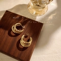 Detailweergave van drielaagse vergulde oorringen op een minimalistisch houten display - B-515 Drievoudige Ring / Goud