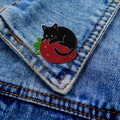 Detail of a cartoon black cat on a red strawberry enamel pin pinned on blue denim fabric - Black Cat Strawberry-Silver Edge