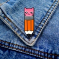 Detalle de broche esmaltado de gato rosa y lápiz naranja sobre tela vaquera azul - Gato Rosa Lápiz