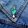 Close-up of zombie hand enamel pin with V sign and bandages on blue denim jacket - Zombie Hand (040-3-21)