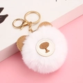 Detail of white faux rabbit fur pom pom keychain with brown bear ears on pink background - White