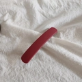 Dettaglio di un fermaglio per capelli in acrilico rosso opaco su fondo in tessuto bianco - Rosso