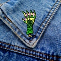 Close-up of a colorful monster claw enamel pin pinned to a blue denim jacket pocket - Monster Hand