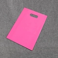Flat lay rose pink PE plastic shopping bag with oval die-cut handle on grey fabric - Pink
