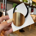 Detail of a minimalist gold brushed metal oval ornament on a black elastic hair tie - Large Oval