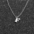 Macro shot of silver stainless steel letter F pendant on a delicate chain necklace - Steel F
