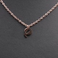 Macro view of polished rose gold letter Q pendant on O-chain over black leather - Rose Gold Q