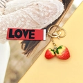 Schattige aardbei sleutelhanger met LOVE stoffen label en gouden ring op gele achtergrond - LOVE Dubbele Aardbeien