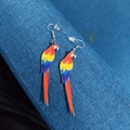Macro shot of colorful acrylic macaw parrot earrings on a blue textured background - Red Macaw