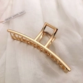 Detailed view of a large golden metal hair claw clip with a strong spring on white fabric - KC Gold-Straight